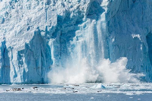 海面に浮かぶ巨大な氷山が崩れ落ちる写真